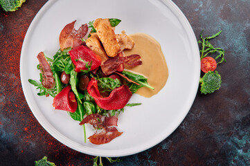 Warm salad with chicken and bacon on white plate on blue oxidized background. Dish for the menu. Top view