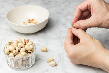 Hands opening a roasted salted pistachio over a marble table