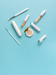 White makeup cosmetics on a blue background with copy space. On the table are shadows, mascara, brushes, lipstick, top view