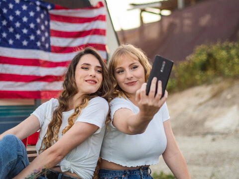 Amigas habiéndose un selfie con la bandera de Estados Unidos de fondo disfrutando el Día de la Independencia de los Estados Unidos