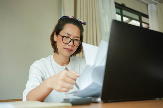 close up young adult asian woman checking or reading monthly report from company while work from home at house with stress and headache emotion for unhealthy lifestyle concept