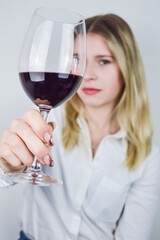 Portrait of a beautiful young blonde woman who raises a glass of red wine to appreciate its color and nuances at a wine tasting - Focus on the glass of wine	