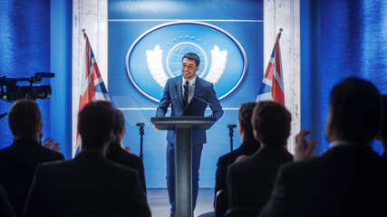 Young Organization Representative Speaking at Press Conference in Government Building. Press Officer Delivering a Speech at Summit. Minister Speaking to Congress. Backdrop with Great Britain Flags.
