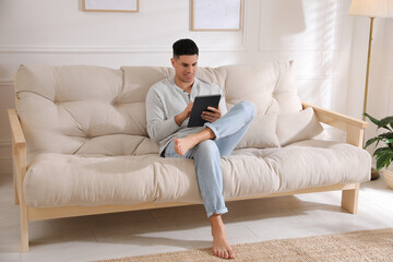 Obraz premium Man using tablet on sofa at home