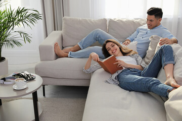 Happy couple with book on sofa in living room - Powered by Adobe