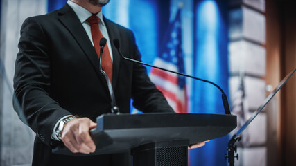 Close up of Organization Representative Speaking at a Press Conference in Government Building. Press Officer Delivering a Speech at a Summit. Minister at Congress. Backdrop with American Flags. - obrazy, fototapety, plakaty