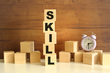 Five wooden cubes stacked vertically on a brown background make up the word SKILL.
