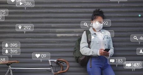 Animation of social media icons and numbers on banners over woman in face mask using smartphone - Powered by Adobe