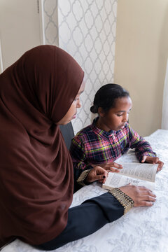 Black Muslim mother and daughter reading on the kitchen table 