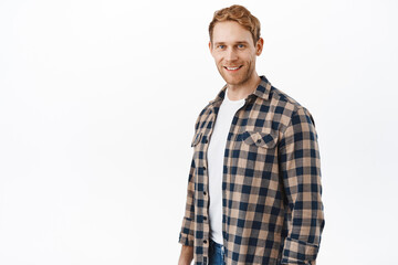 Attractive caucasian man with red hair and blue eyes, looking happy at camera, smiling and standing casual against white background