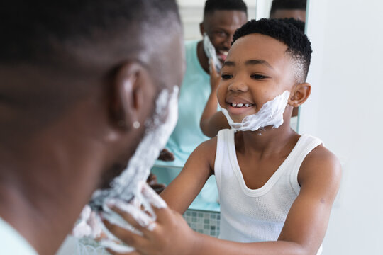 African american father and son in bathroom, applying shaving foam