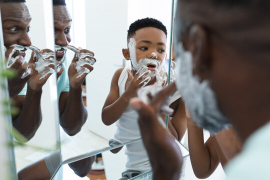 African american father and son in bathroom, applying shaving foam