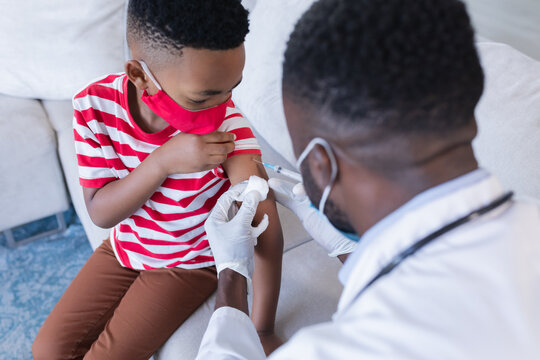 African american male doctor wearing face mask vaccinating boy patient