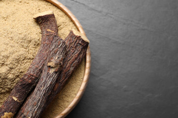 Powder in bowl and dried sticks of liquorice root on black table, top view. Space for text