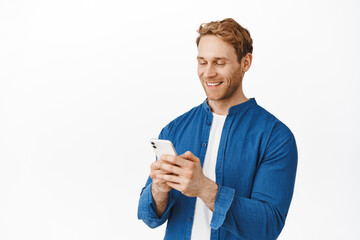 Modern candid guy with phone in hands chatting, message or read screen, smiling at smartphone display while using application, standing over white background - 433615052