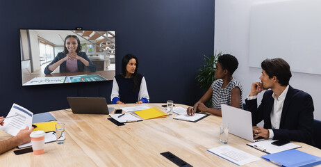 Diverse group of business colleagues having video call with businesswoman on screen in meeting room