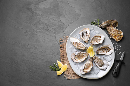 Delicious fresh oysters with lemon slices served on black slate table, flat lay. Space for text