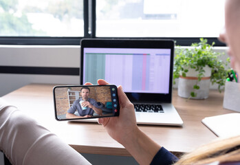 Caucasian woman sitting at desk using smartphone having video call with coworker