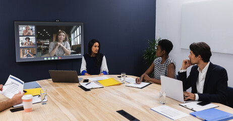 Diverse group of business colleagues having video call with coworkers on screen in meeting room