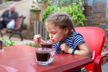 Child girl sitting at the table sips hot tea from a teaspoon