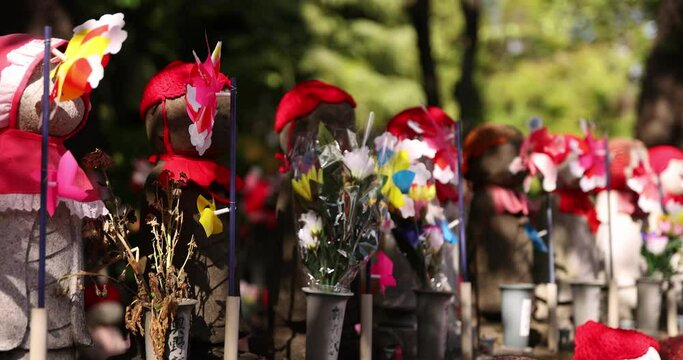 A slow motion of moving colorful windmills with Jizo statue daytime closeup