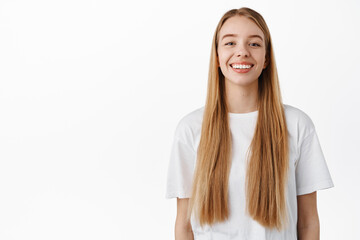 Portrait of young woman with long healthy blond hair, smiling with white perfect teeth, standing in...