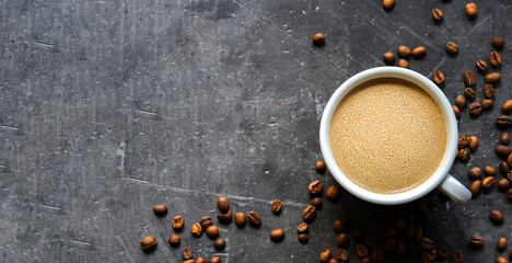 Horizontal banner with a cup of coffee and coffee beans on a dark concrete background. Top view. Copy space. Espresso or Americano in a cup.