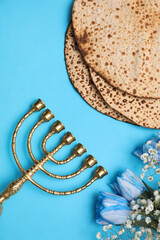 Tasty matzos, flowers and menorah on light blue background, flat lay. Passover (Pesach) celebration