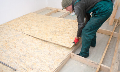 Man worker fits wooden oriented stands bords on insulated floor. New house constuction
