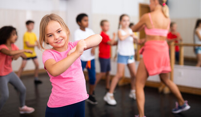 Smiling little girl training movements of vigorous dance with group of tweens in children dance studio