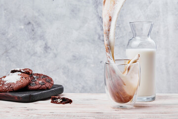Splash of coffee with milk in a transparent glass. Chocolate cookies and glass of milk on light concrete background. Photo for menus and advertising. Space for text