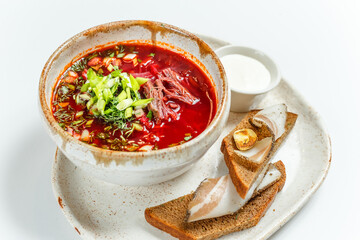 bright juicy red soup borscht with green onions, croutons and bacon with garlic, on a light background, close-up