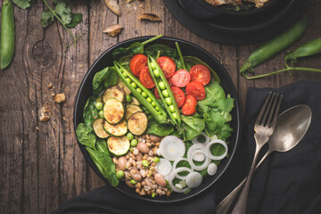 Healthy dinner, lunch. Vegetarian Buddha bowl or healthy salad with balanced ingredients. Spinach, grilled zucchini, grains, beans, green onions, cherry tomatoes and fresh peas served. Rustic style