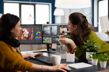 Coworkers video editors discussing in front of pc working for client footage using post production...