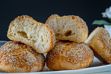 Fresh challah bread rolls hot from the oven cut into half. Crumb shot of gluten free bread buns or mini loaves with sesame seeds and golden color. Fluffy homemade bread, dark background with flowers