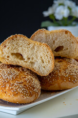 Fresh challah bread rolls hot from the oven cut into half. Crumb shot of gluten free bread buns or mini loaves with sesame seeds and golden color. Fluffy homemade bread, dark background with flowers