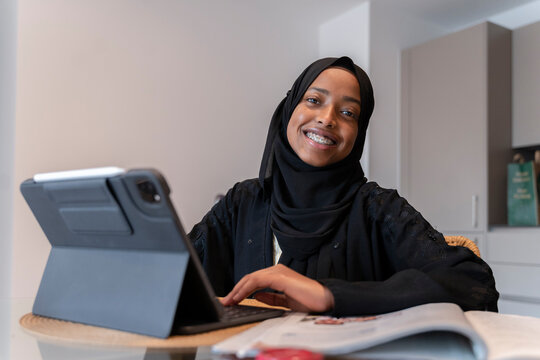 Black Muslim teenage girl doing work on a small electronic device 