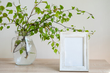 Portrait white picture frame mockup on wooden table Modern glass vase with green branches White wall background Scandinavian interior Eco lifestyle