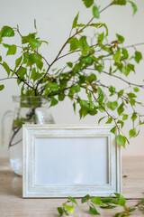Portrait white picture frame mockup on wooden table Modern glass vase with green branches White wall background Scandinavian interior Eco lifestyle
