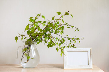 Portrait white picture frame mockup on wooden table Modern glass vase with green branches White wall background Scandinavian interior Eco lifestyle