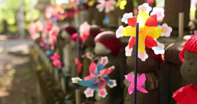 A slow motion of moving colorful windmills with Jizo statue daytime closeup