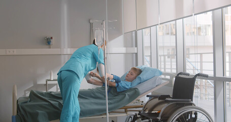 Female nurse setting up iv drip for sick little boy lying in hospital bed