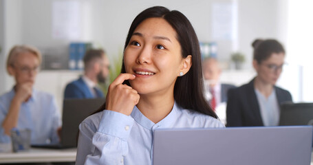 Asian businesswoman working on laptop at desk in open space office.