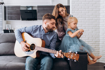 Family plays the guitar. Father plays the guitar for his wife and daughter.