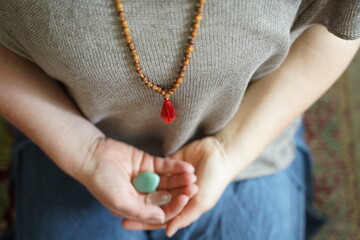 hands of a woman holding stones with upper body wearing a mala 