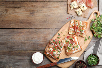 Delicious sandwiches with prosciutto, cheese and microgreens on wooden table, flat lay. Space for text