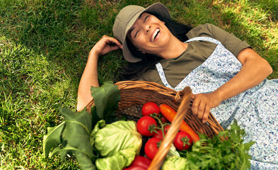 View from above of a gorgeous female gardener lying on the grass with a basket with freshly picked...