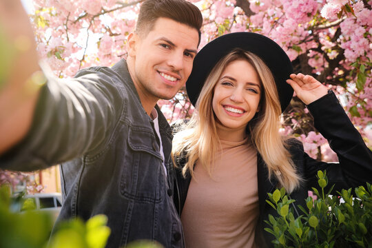 Happy couple taking selfie near blossoming sakura outdoors on spring day