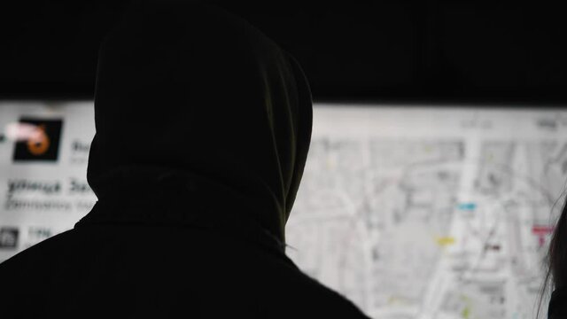 The guy in the hood looks at a large light map of the city hanging on the wall in the subway. Close-up shooting