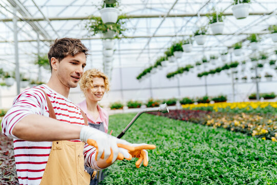 Young handsome experienced plantation worker showing new colleague which plants to water.
